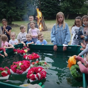 W dużym zbiorniku wodnym pływają wianki z kwiatów, wkoło zbiornika stoją dzieci.