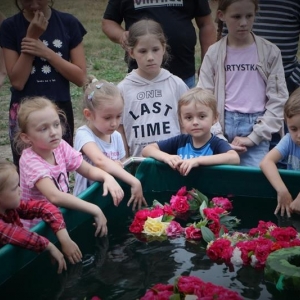 Grupa dzieci stoi przy zbiorniku wodnym. W zbiorniku pływają uplecione wianki.