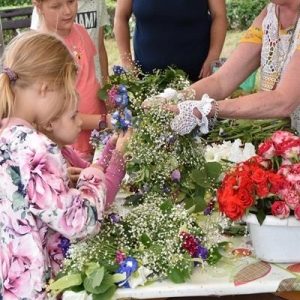 Na stole leżą bukiety żywych kwiatów, obok stolika stoi grupka dzieci.