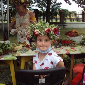 Dziewczynka w wianku na głowie z białych i czerwonych kwiatów pozuje do zdjęcia.