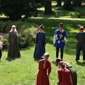 Grupa osób w średniowiecznych strojach stoi w parku, obok stoi mały chłopczyk.