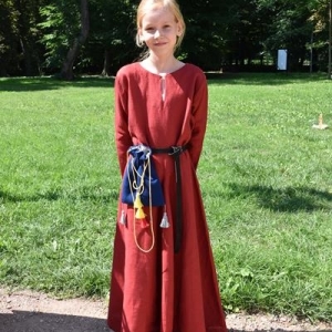 Dziewczynka w średniowiecznym stroju pozuje do zdjęcia.W tle parkowe drzewa.