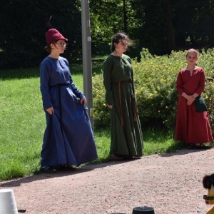 Trzy dziewczęta w strojach sredniowiecznych stoją na tle zielonych drzew.