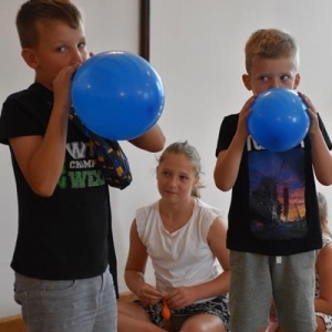 Dwóch chłopców dmucha balony.W głębi siedzi dziewczynka.