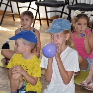 Grupa dziedzi dziewczynki i chłopiec siedza na podłodze, w dłoniach mają nadmuchane balony.