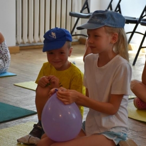 Mały chłopiec i dziewczynka trzymaja w dłoniach nadmuchany balon.Dzieci znajdują się w sali.