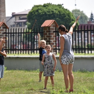 Trójka dzieci stoi na dworze i słucha osoby dorosłej, która pokazuje dłonią prawy kierunek.