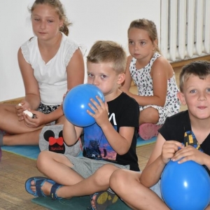 Dwóch chłopców trzyma w dłoniach nadmuchane balony, obok nich siedza dwie dziewczynki.