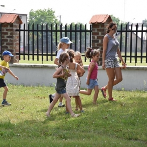 Grupa dzieci biega po trawie , na otoczonym terenie.