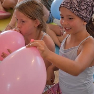 Dwie usmiechnięte dziewczynki trzymaja w dłoniach nadmuchane balony