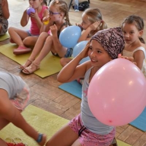 Grupa  rozesmianych dzieci siedzi na matach w sali .Każde dziecko trzyma w dłoniach nadmuchane balony.
