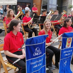 Orkiestra dęta ZHP - OSP Uniejów. Na pierwszym planie na krzesłach siedzą trzy dziewczęta .