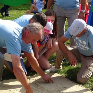Piknik Sołtysów. Na ziemi wysypany jest piasek. Czterej mężczyźni w niebieskich koszulkach rysują kontur na piasku. 
