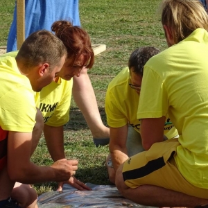  Piknik Sołtysów .Grupa kobiet i mężczyzn siedzi na ziemi i rysuje na rozłożonej foli kolorowymi pisakami.