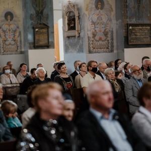 Grupa mężczyzn i kobiet  słucha koncertu w kościele.