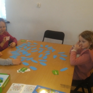 Trzy małe dziewczynki siedzą przy stoliku, na stoliku niebieskie kartoniki.