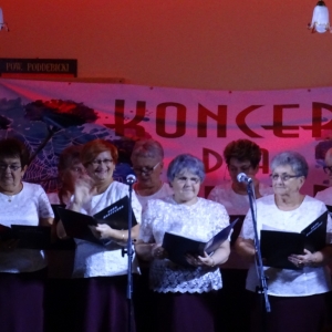 Grupa kobiet z zespołu śpiewaczego stoi na scenie 