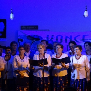 Grupa kobiet z zespołu śpiewaczego stoi na scenie i śpiewa piosernkę