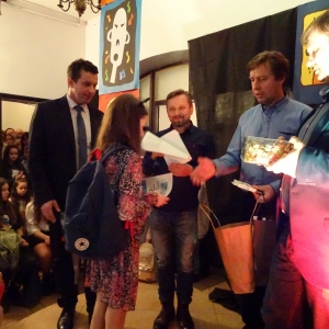 Dziewczynka w kolorowej sukience z plecakiem odbiera nagrody i dyplom od czterech jurorów