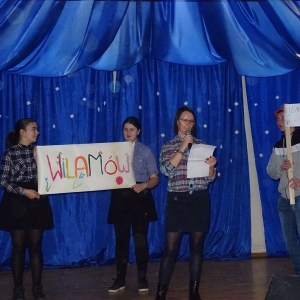 Grupa osób stoi na scenie, dwie kobiety trzymająplansze z napisem, obok kobieta z mikrofonem.