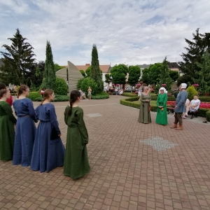 Grupa kobiet w długich sukniach stoi na placu.