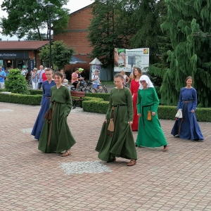 Zespół kobiet w średniowiecznych strojach tańczy.
